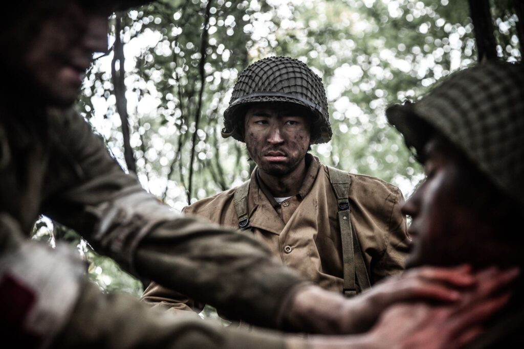 Private Barney Hajiro watches a Medic treat his friend, Private Onaga's bullet wound. (Dramatic Recreation) L-R: Gabriel Prevost, Kristopher Hori, Sei Campbell