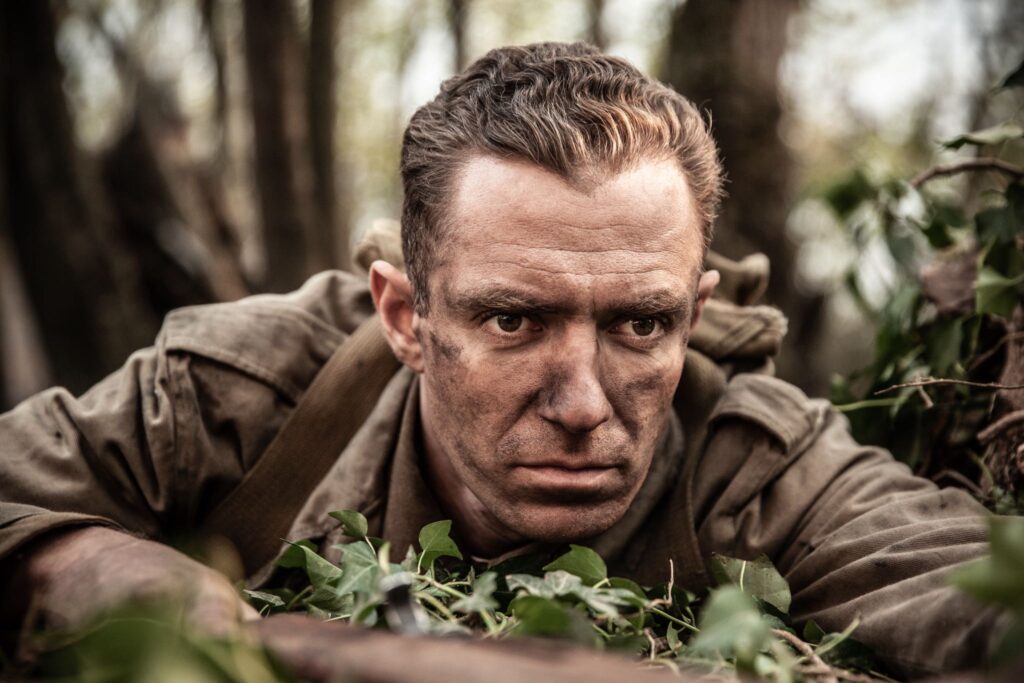 Ignoring his wounds, 2nd Lieutenant Audie Murphy peers through the underbrush to locate the enemy sniper. (Dramatic Recreation) (William Redfern)